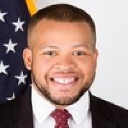 Dr. Marvin Carr, a Black man with a beard wearing a red tie in front of the American flag