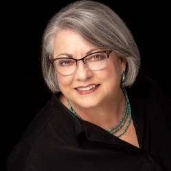 Headshot of Tara Sandercock wearing a black shirt and a blue necklace and glasses.